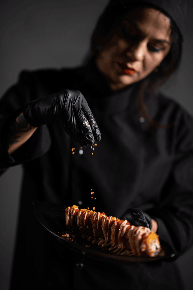 femme qui met des épices sur de la viandes avec des gans noir. Photo assez sombre